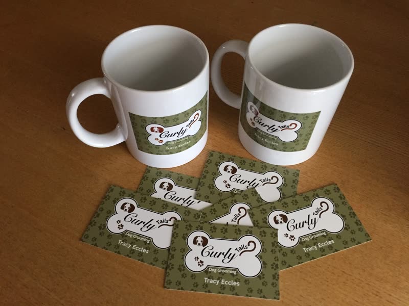 Branded mugs and a fan of bone-shaped Curly Tails business cards on a wooden table